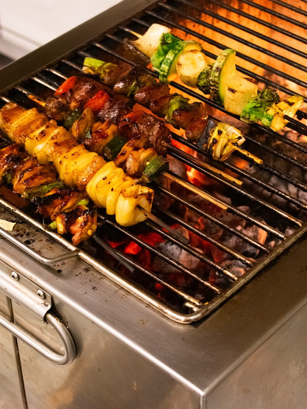 Espetos de carne, frango e legumes grelhando sobre a brasa na cozinha do Vague.