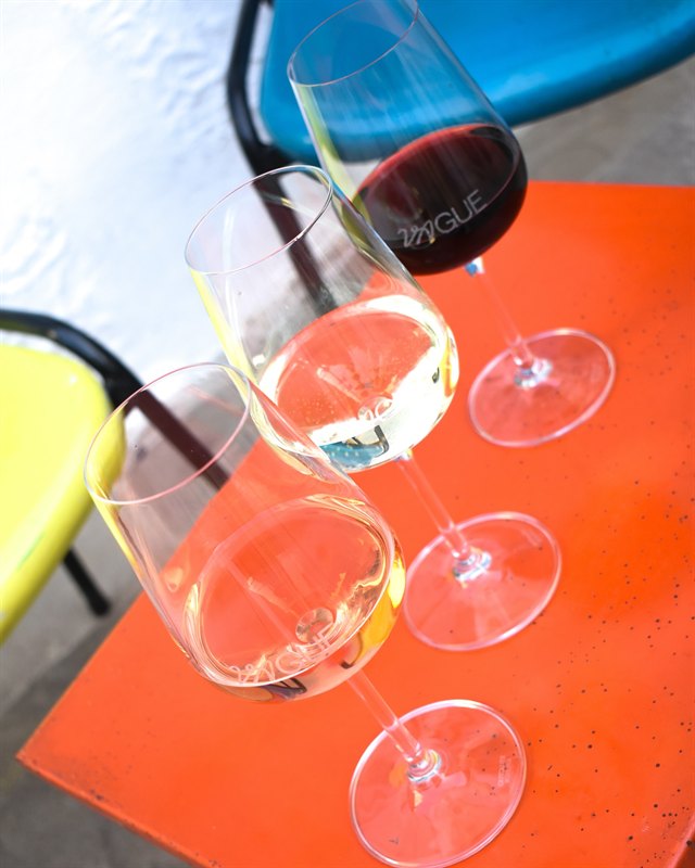 Taças de vinho gravadas com o nome Vague sobre uma mesa laranja.